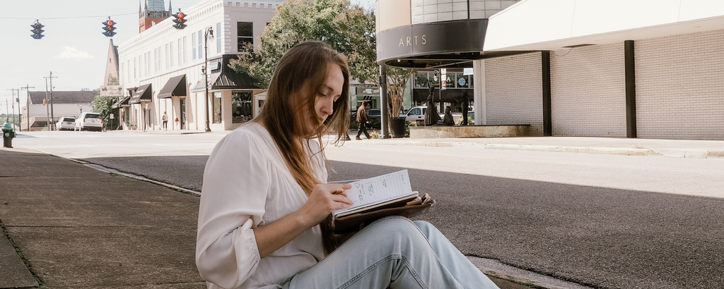 Shelby uses her planner while sitting on a sidewalk in the city.
