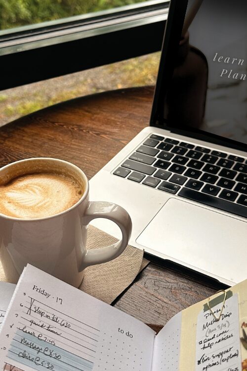 An open planner, coffee, and laptop on a desk