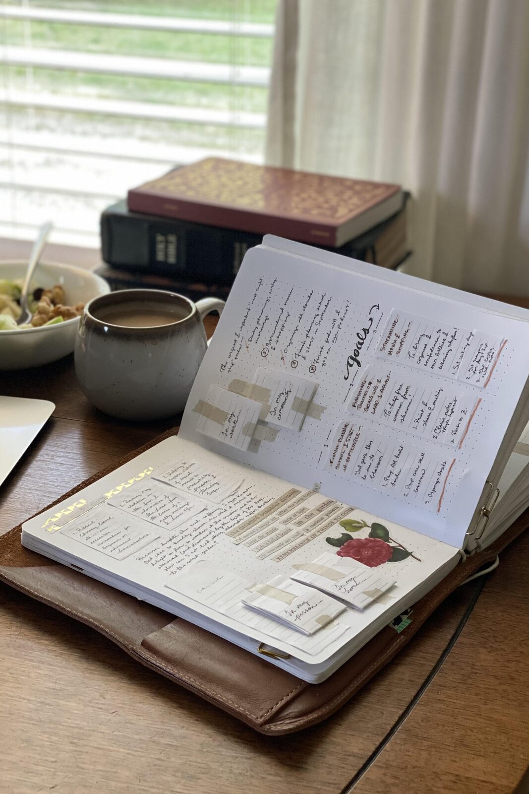 A journal page titled “Goals,” open beside a stack of books and a cup of coffee